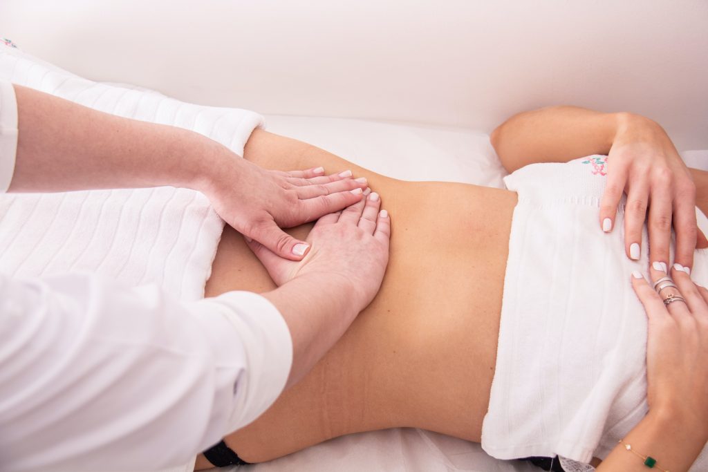 A woman performs manual lymphatic drainage massage by applying very gentle pressure to another woman's belly just above the cisterna chyli