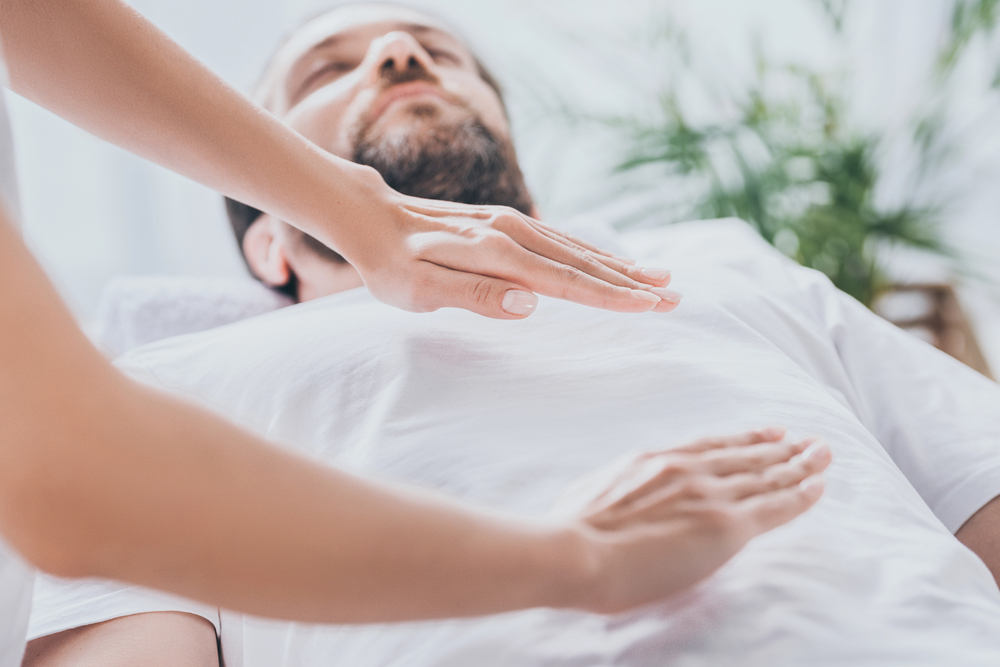 Energy healing practitioner holding hands above a client’s chest during a calming holistic therapy session focused on balancing the body’s energy.